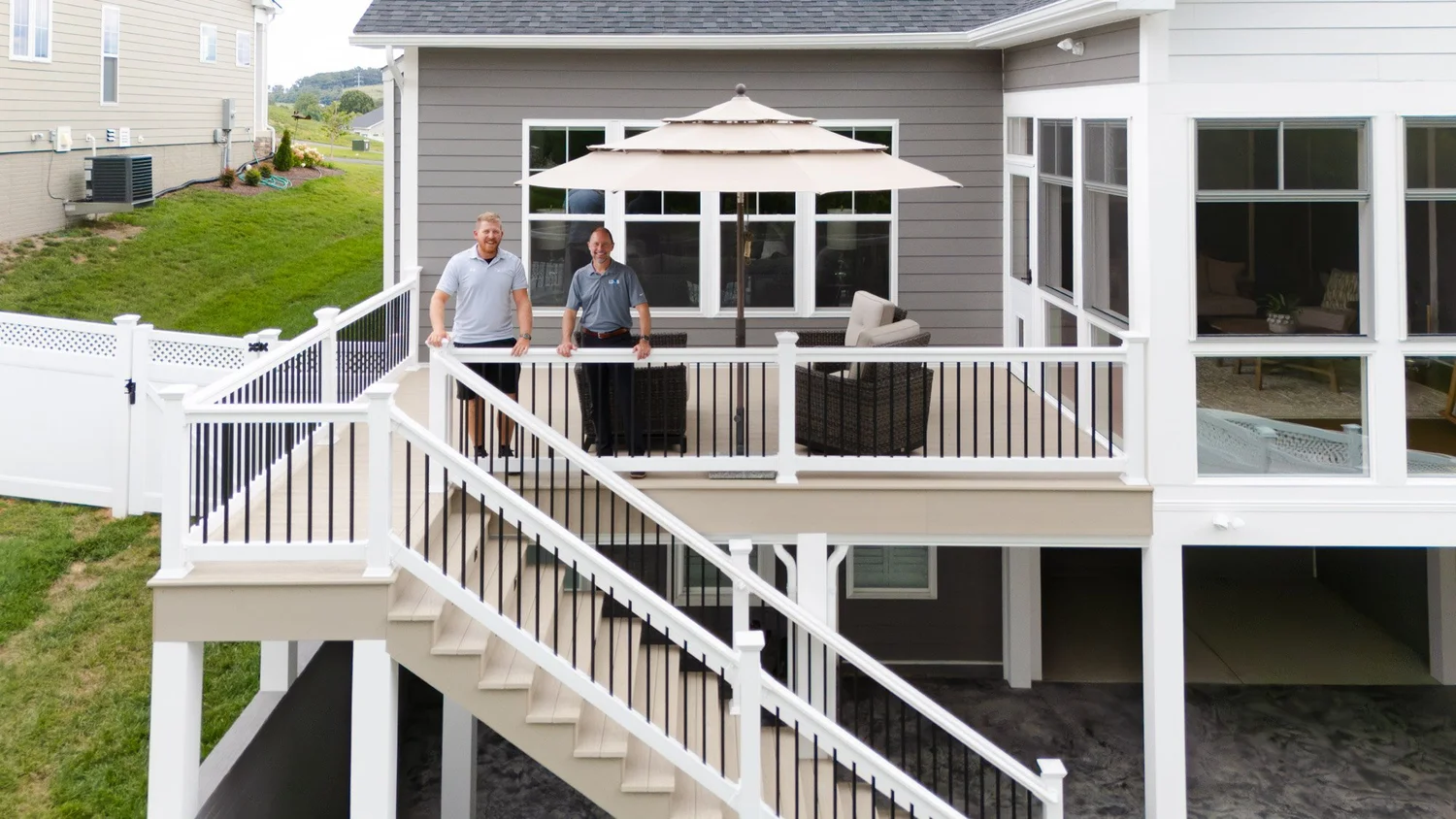 Back of the home with the new deck, stairway and patio umbrella, two men standing at the railing