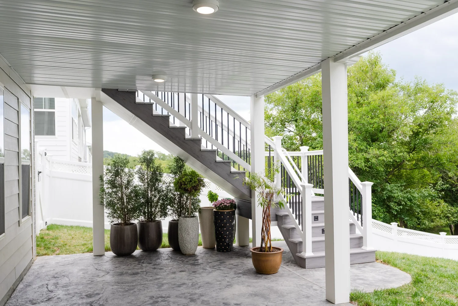 Covered patio under the deck lined with potted plants along the wall