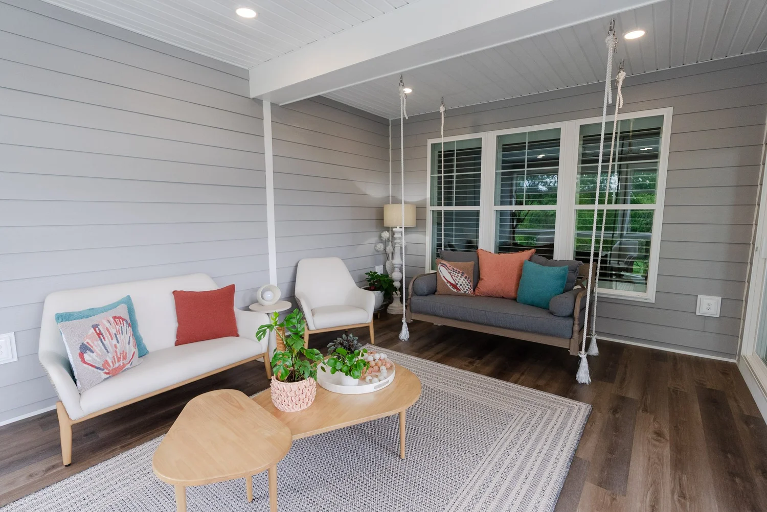 Porch sitting area with white chairs, a woven rug and a rope-hung swing along the wall
