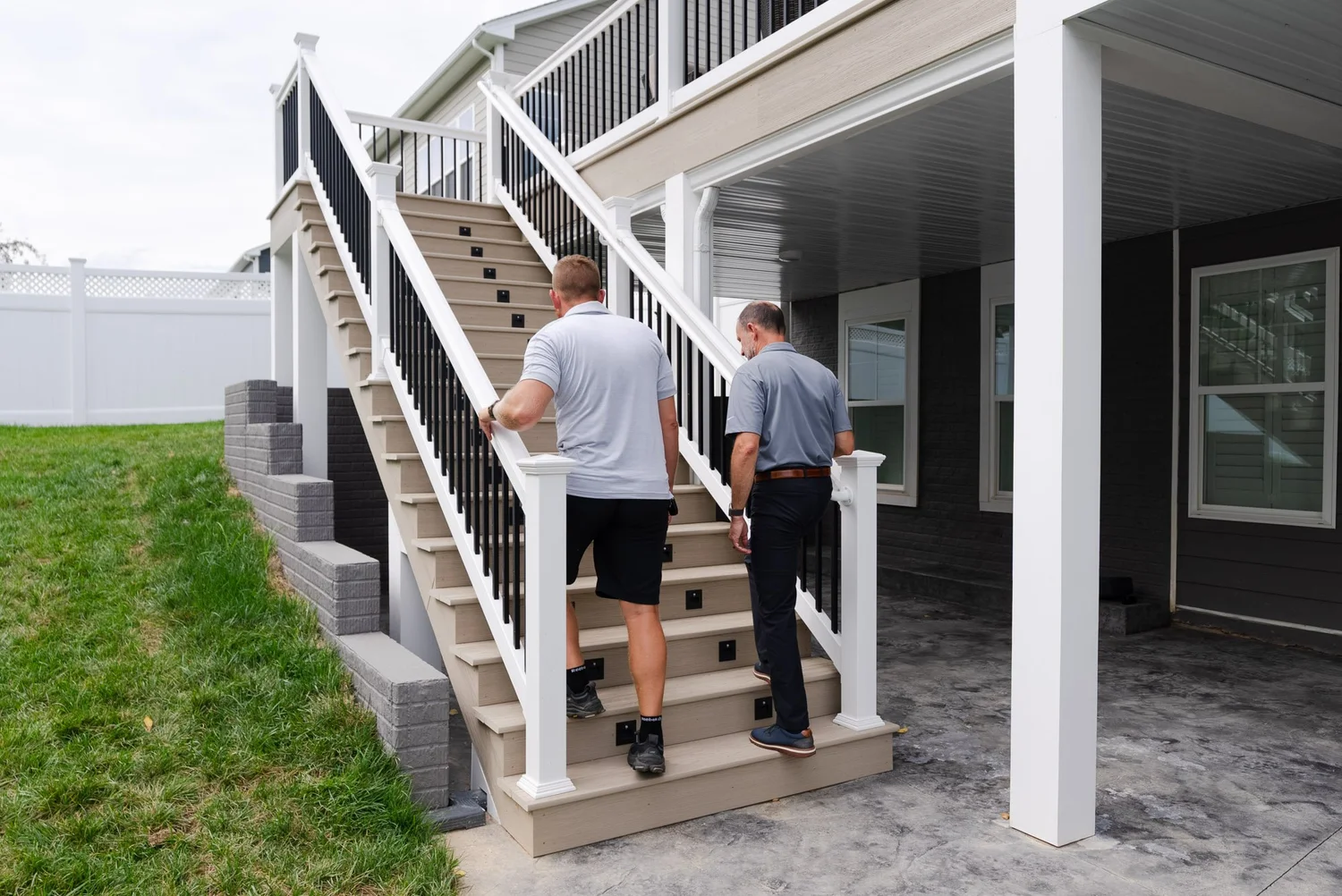 Two men walking up the deck stairs from the stamped concrete patio below