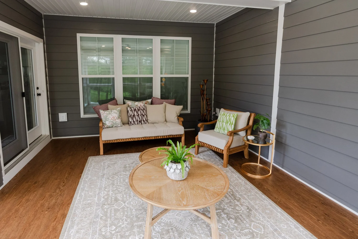 Enclosed porch with gray shiplap walls, a cushioned sofa and a round wood coffee table