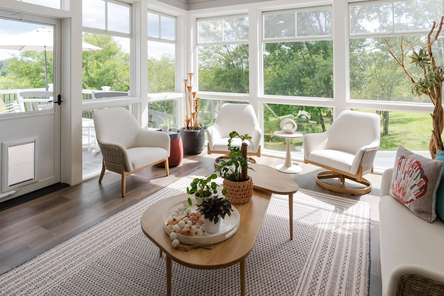 Inside the three-season room with white armchairs, a low table and windows on three sides