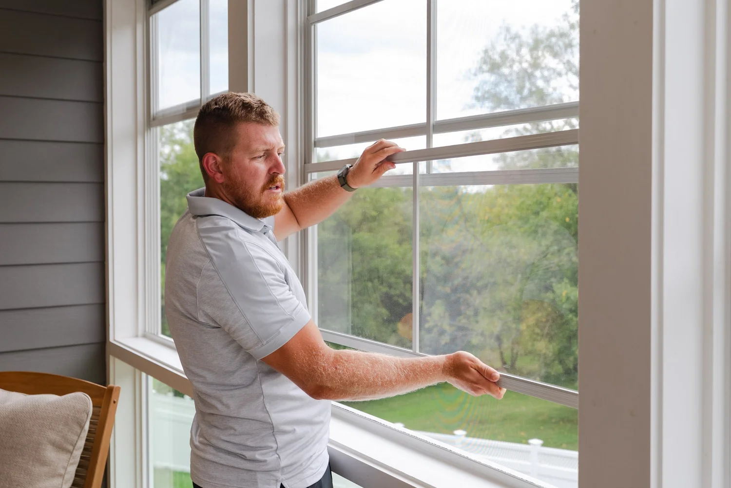 A man sliding a porch window panel back into the track along the top of the frame