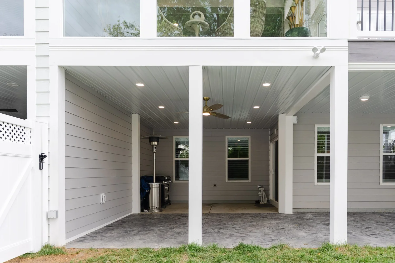 Covered space under the deck with white support posts, a ceiling fan and room for a grill