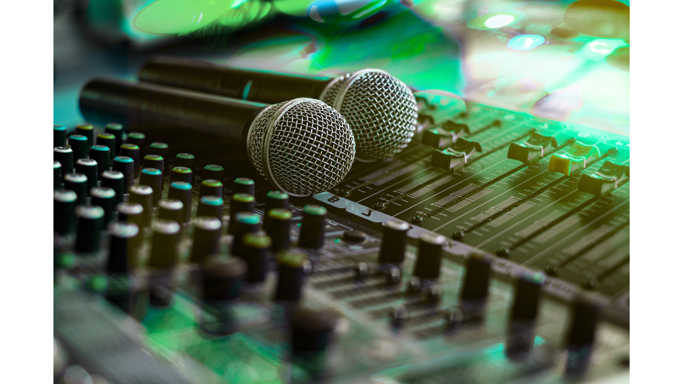 Two microphones placed on a soundboard with various control knobs and sliders, illuminated by green and blue stage lighting.