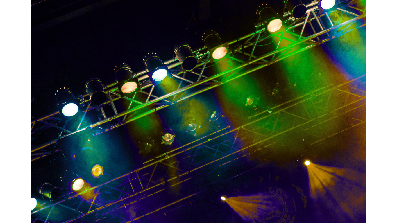 Colorful stage lighting with various spotlights and beams of yellow, green, and white light over a stage or performance area.