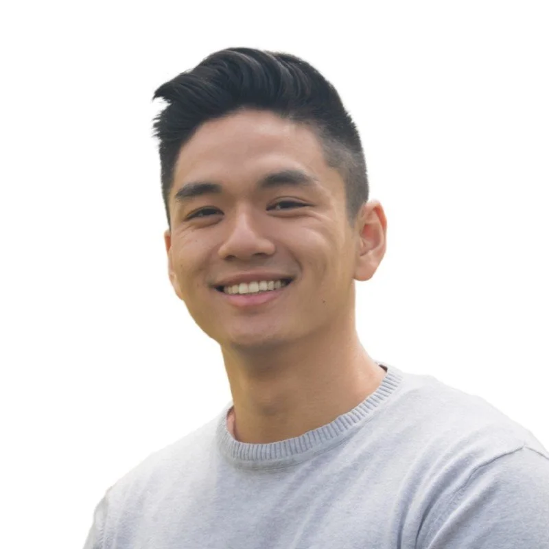 A young man smiling with a short, styled haircut, wearing a light grey shirt, against a white background.