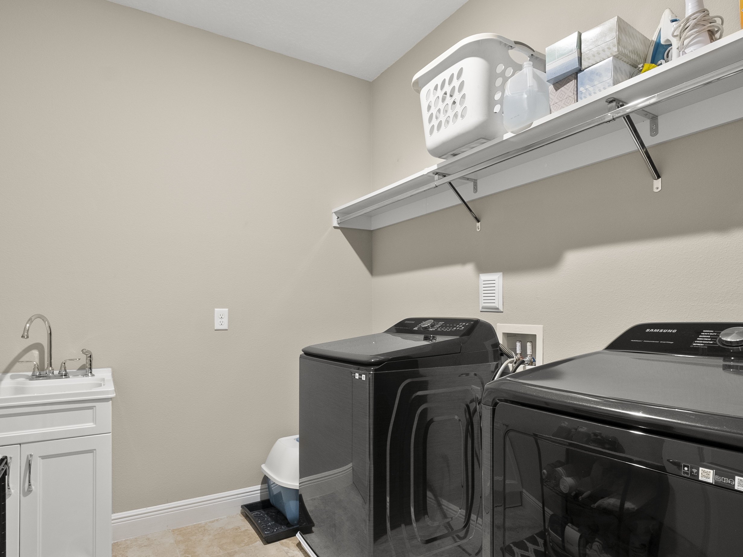 Modern laundry room with washing machine, dryer, utility sink, shelf with laundry supplies and a laundry basket.