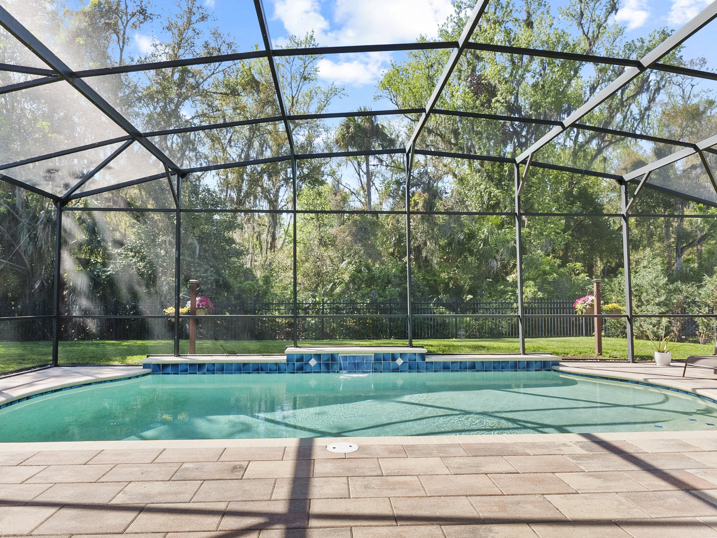 Screened-in outdoor swimming pool with patio and trees in the background.