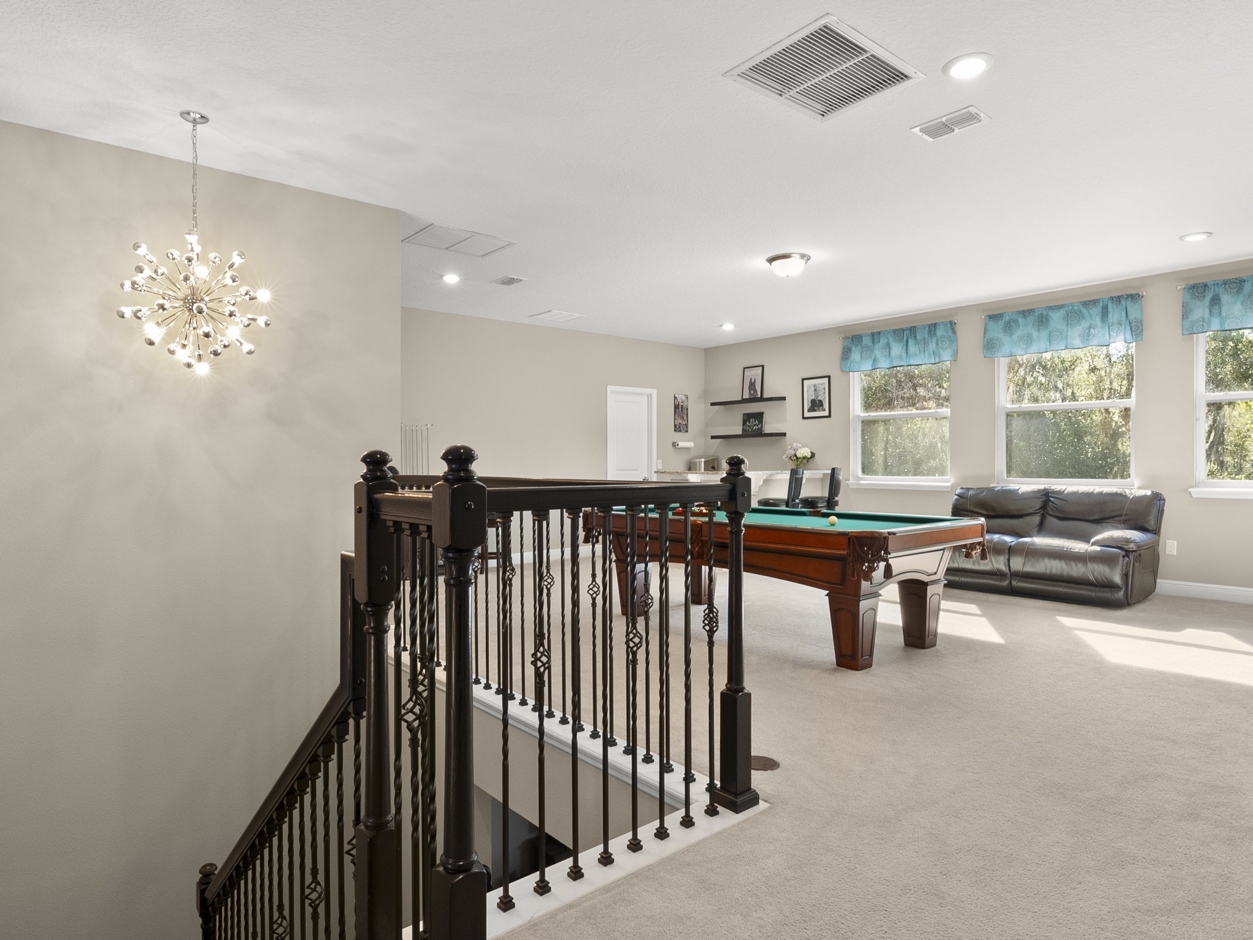 Game room interior with chandelier, pool table, leather sofa, and picture windows.