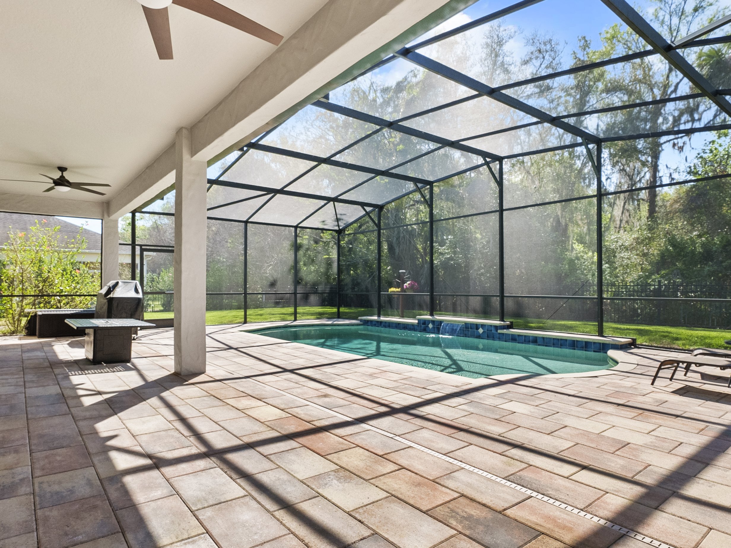 Screened patio with swimming pool, ceiling fans, and outdoor furniture. Overlooking a grassy yard with trees.