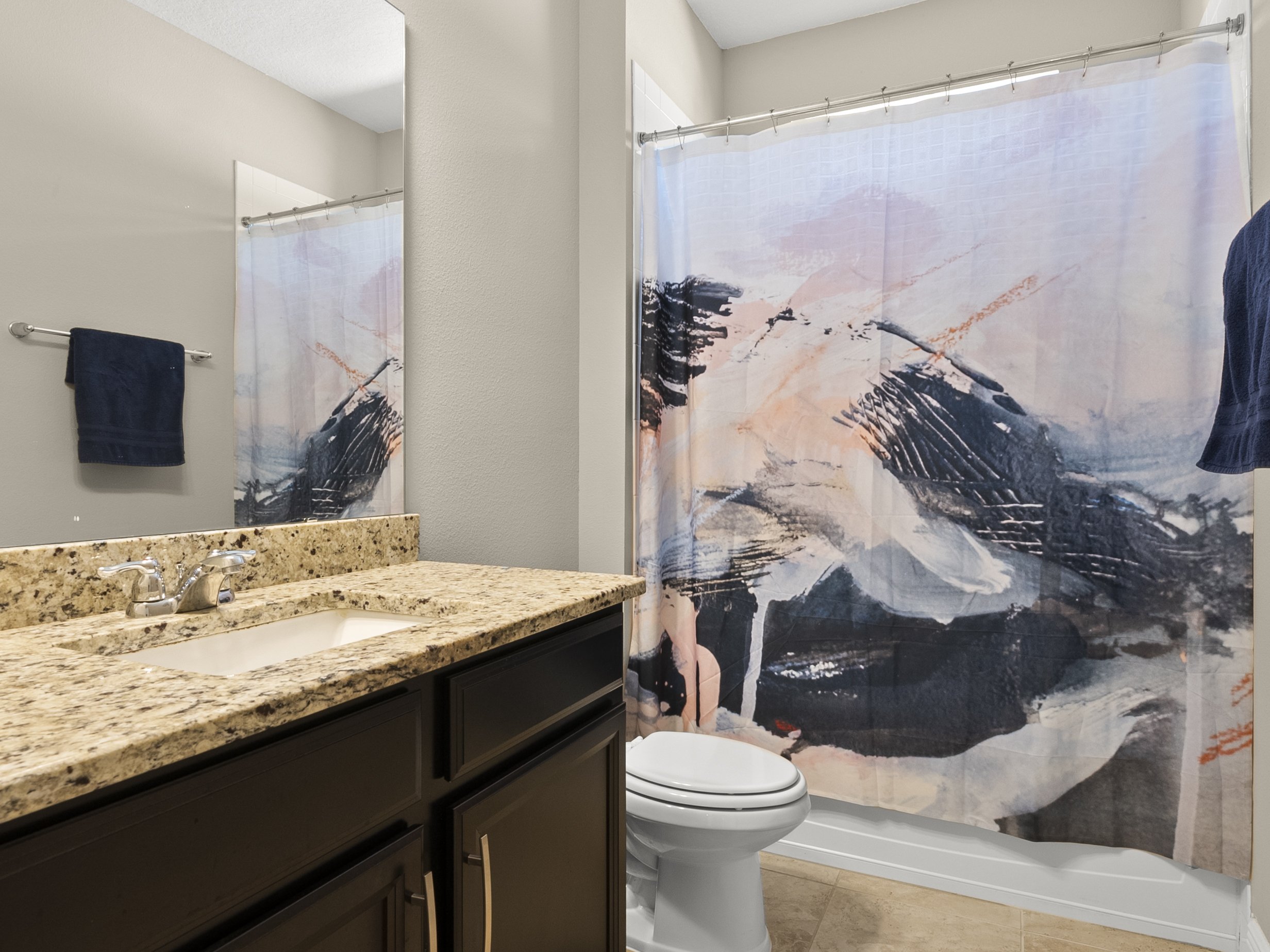 Modern bathroom with abstract design shower curtain, granite countertop, sink, mirror, and black cabinet.