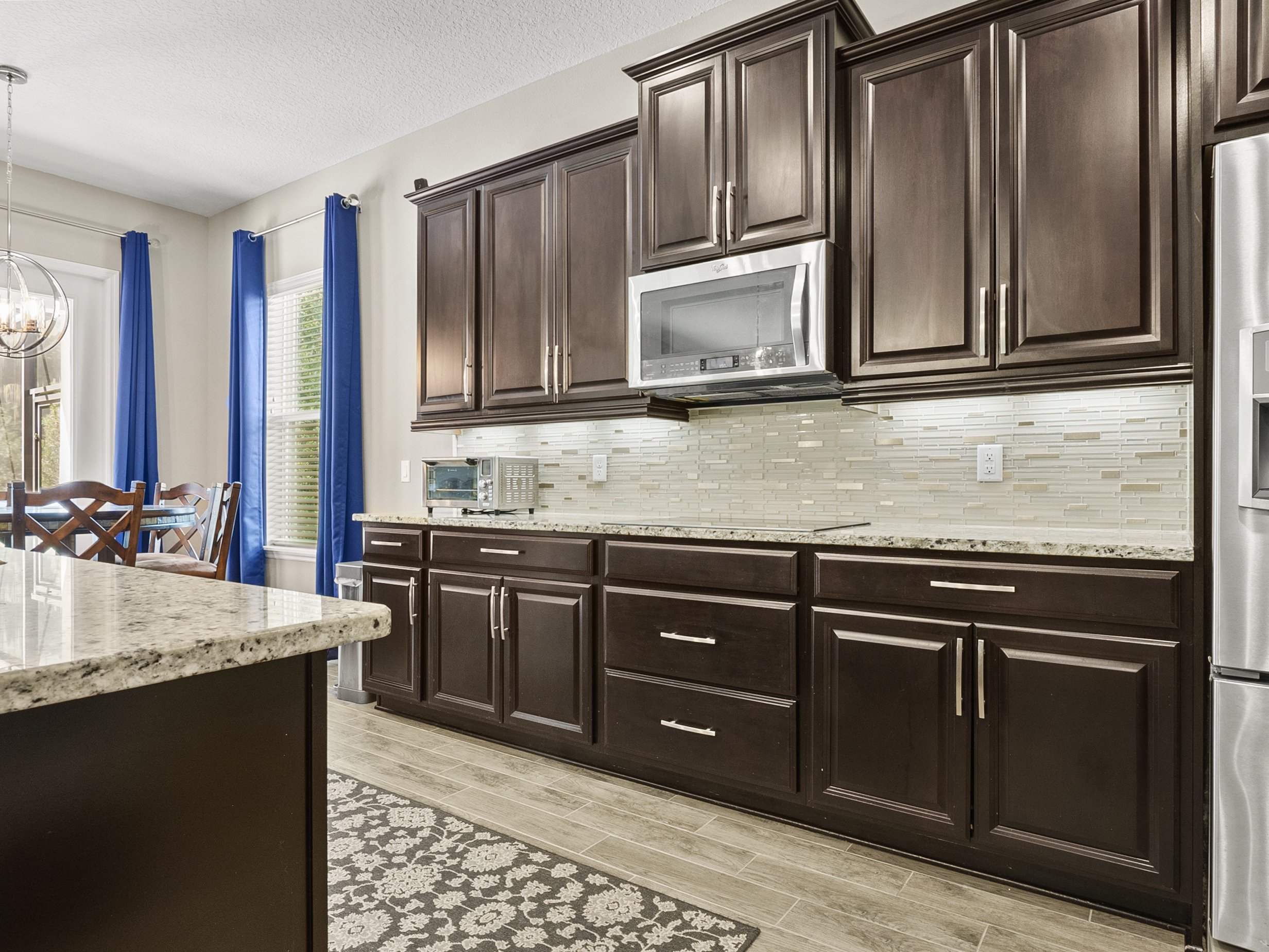 Modern kitchen with dark wood cabinets, granite countertops, stainless steel appliances, and blue curtains