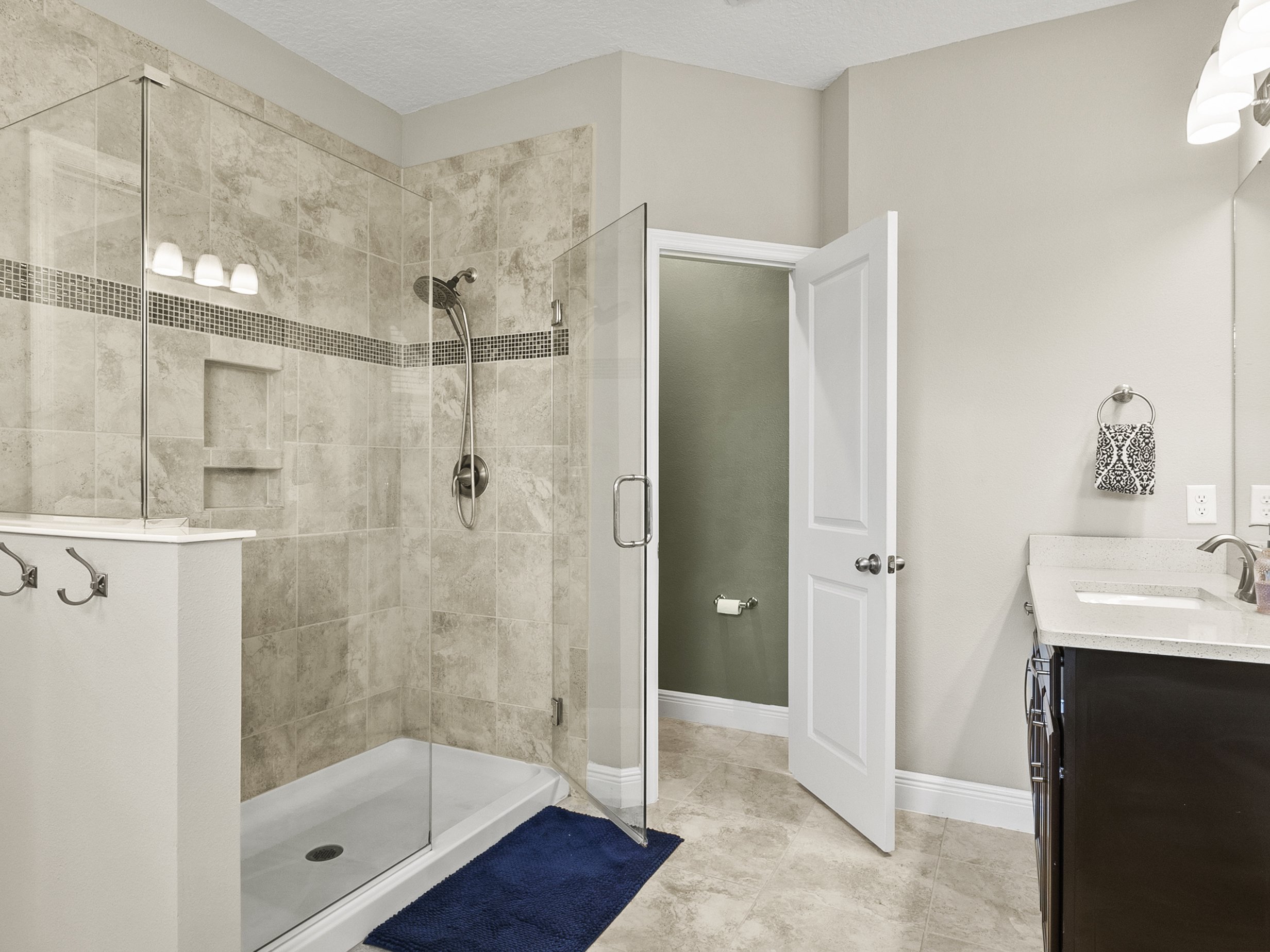 Modern bathroom with glass shower, beige tiled walls, and light vanity countertop.