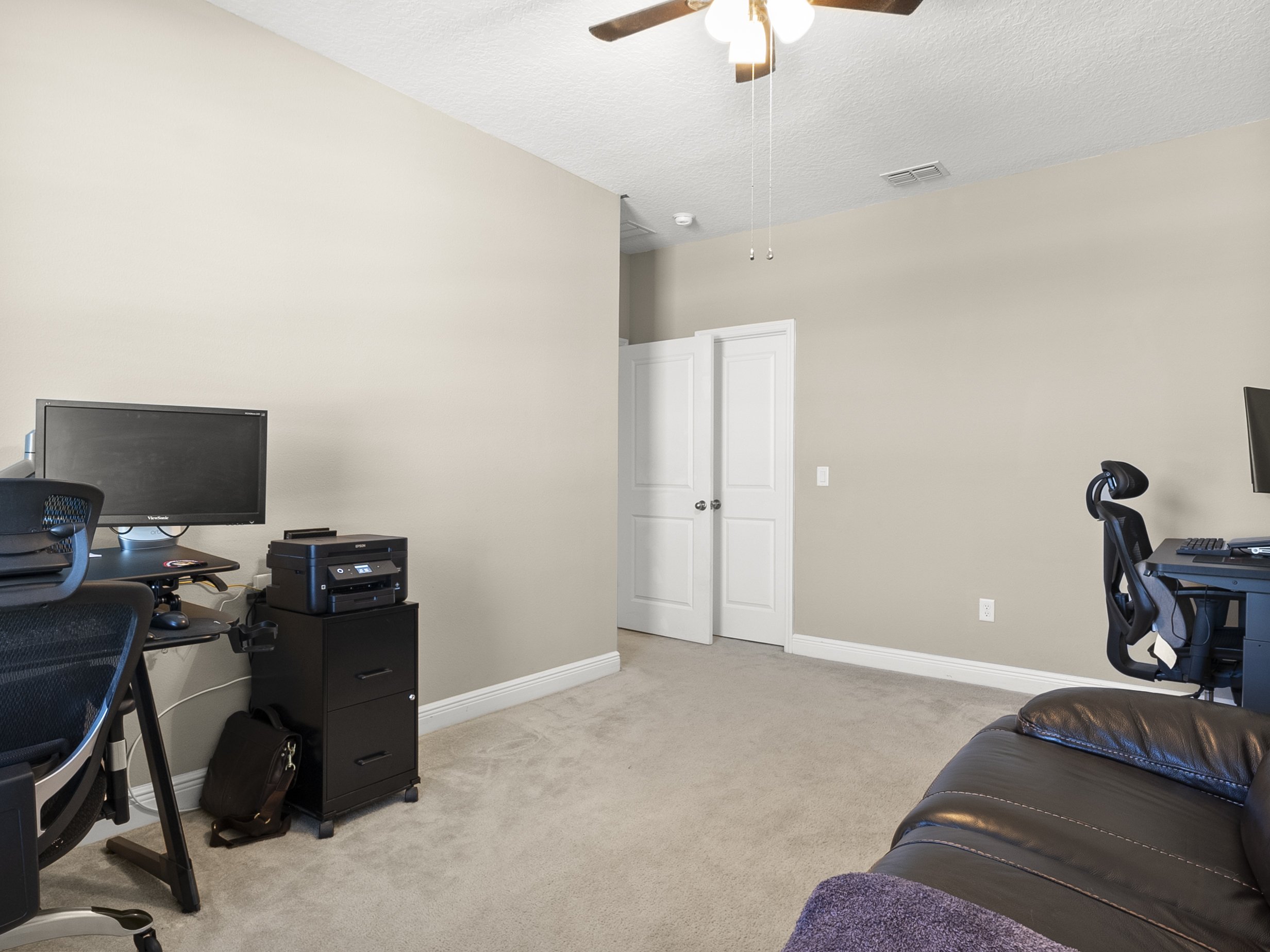 Minimalist office space with two computer desks, chairs, a printer on a cabinet, and a ceiling fan.