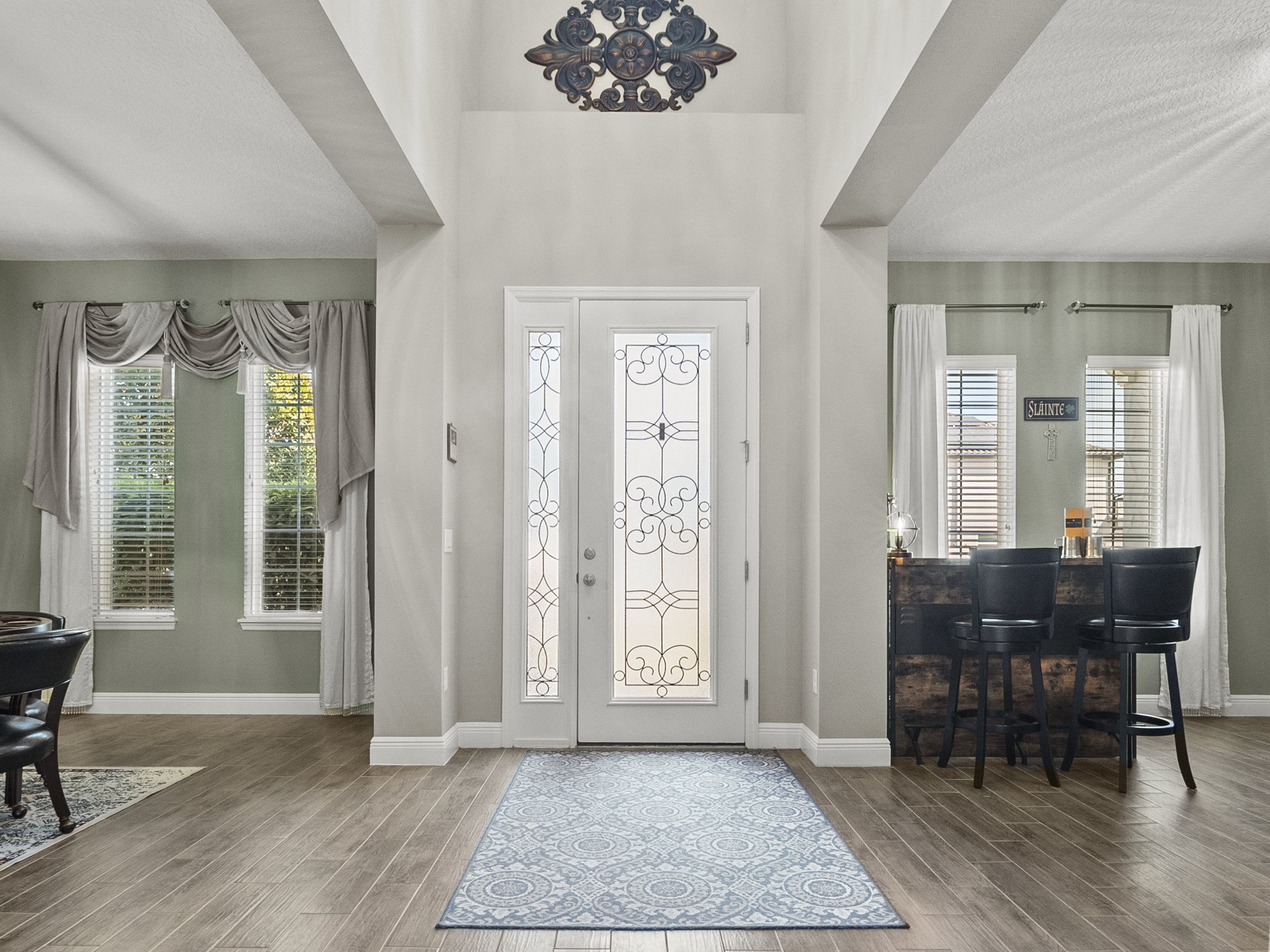 Home entryway with glass paneled door, wood flooring, decorative wall hangings, and a bar area with stools.