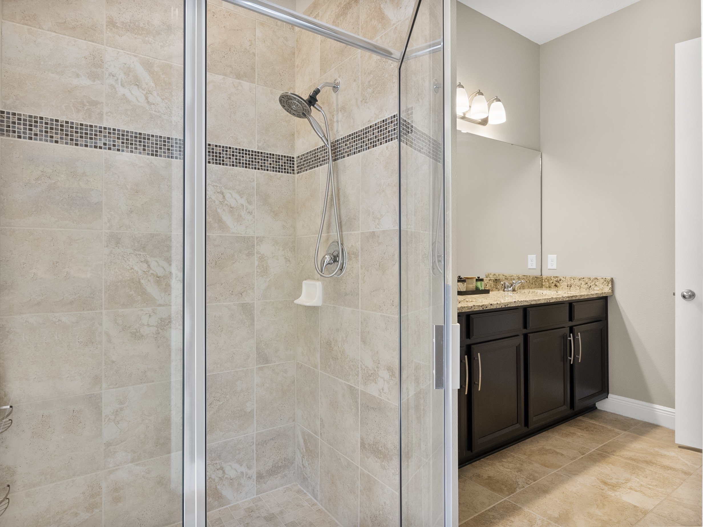 Modern bathroom with a glass-enclosed shower, tiled walls, and vanity with granite countertop.