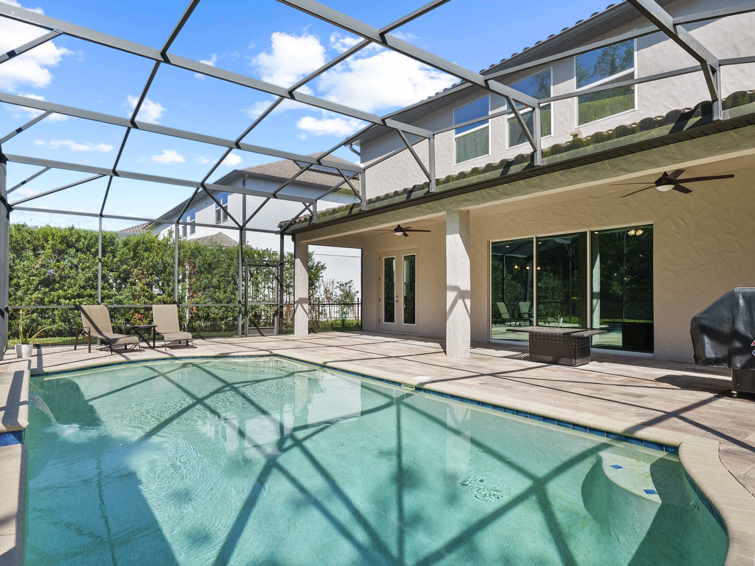 Screen-enclosed backyard with swimming pool, lounge chairs, and a modern house exterior with glass doors and windows.