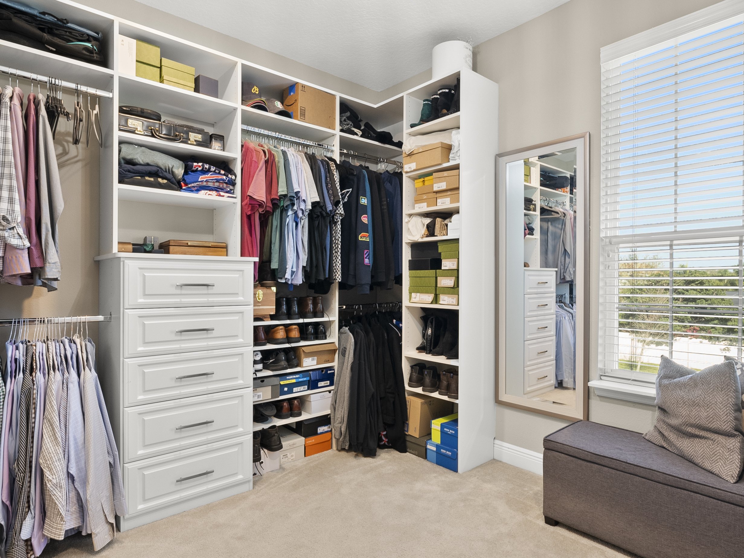 Organized walk-in closet with shelves, hanging clothes, shoes, and a dresser