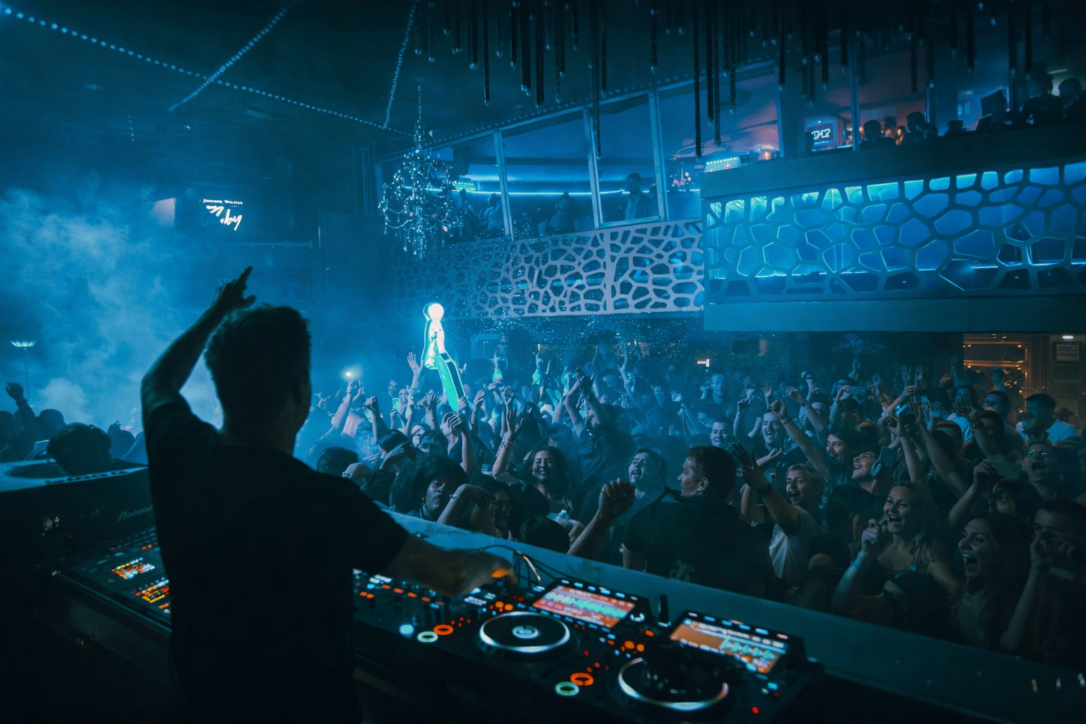 DJ en pleine performance dans un club devant une foule en fête sous des lumières bleues et une ambiance nocturne immersive.