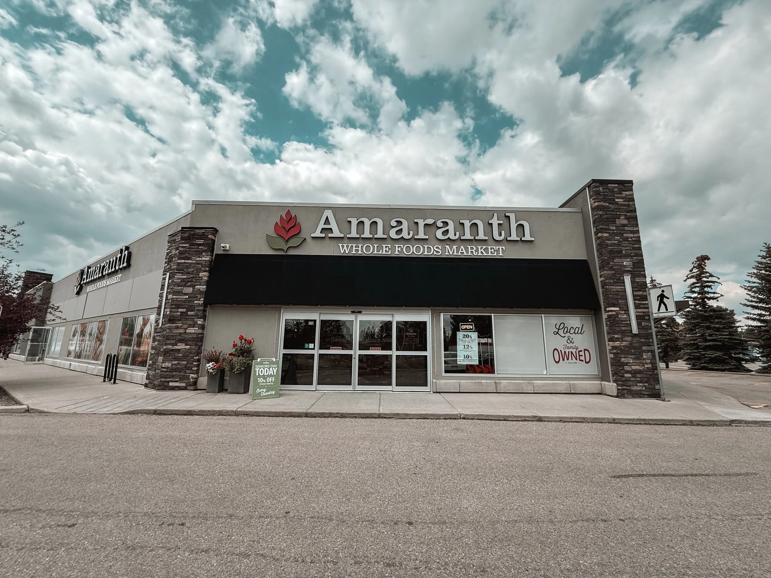 Exterior view of Amaranth Whole Foods Market with a cloudy sky in the background, sidewalk in front, and flower pots near the entrance.
