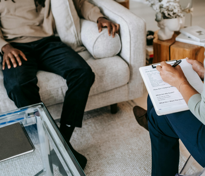 Man on sofa with woman writing on clipboard