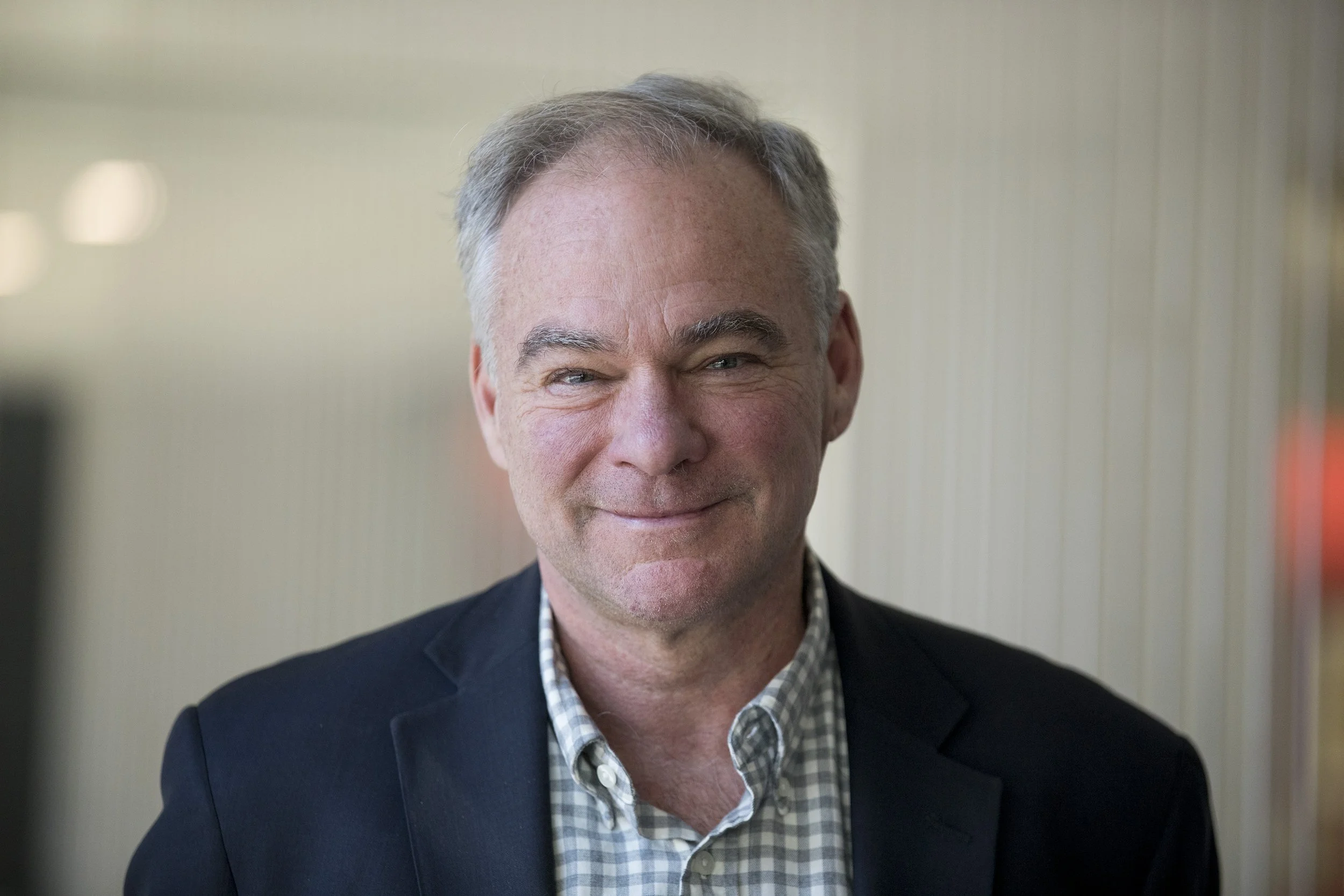 A middle-aged man with gray hair and a smile, wearing a checkered shirt and dark blazer, in an indoor setting.