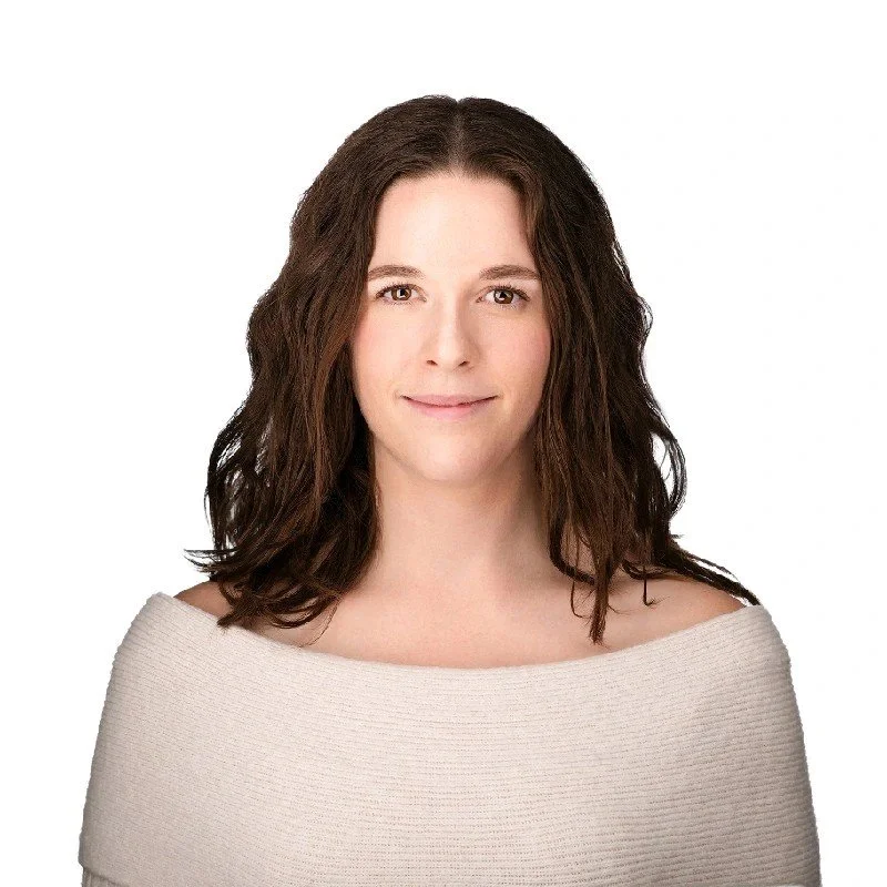 A woman with shoulder-length brown hair and light skin, smiling gently at the camera, wearing a cream-colored off-the-shoulder sweater against a plain white background.