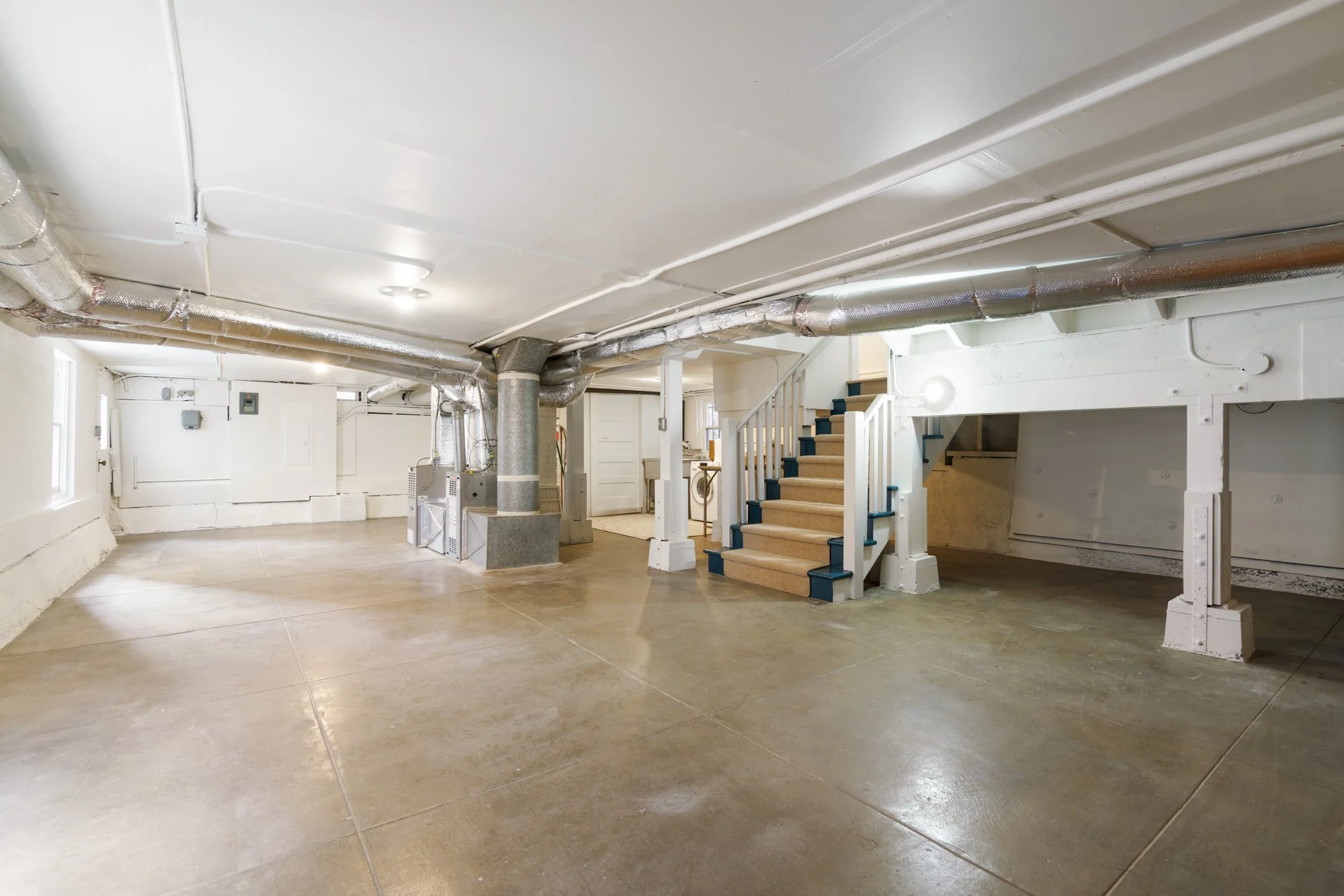 Spacious basement with exposed ductwork, concrete floor, and staircase