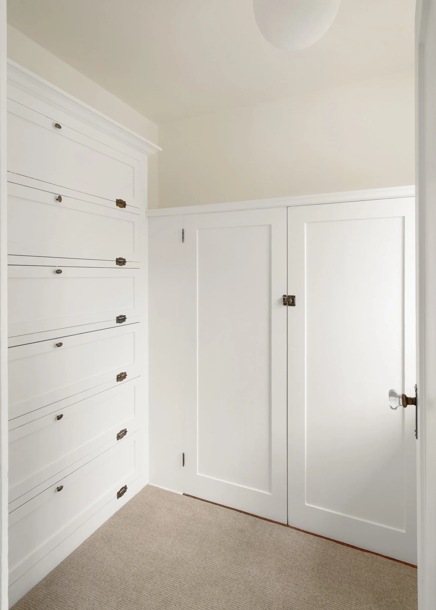White built-in storage cabinets and a closet door with vintage handles, beige carpet flooring.