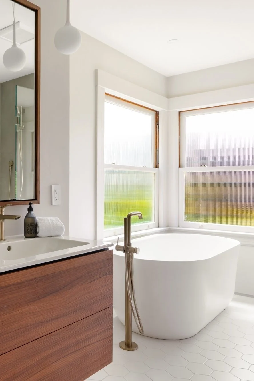 Modern bathroom with freestanding bathtub, wood vanity with countertop, round pendant light, and frosted windows.