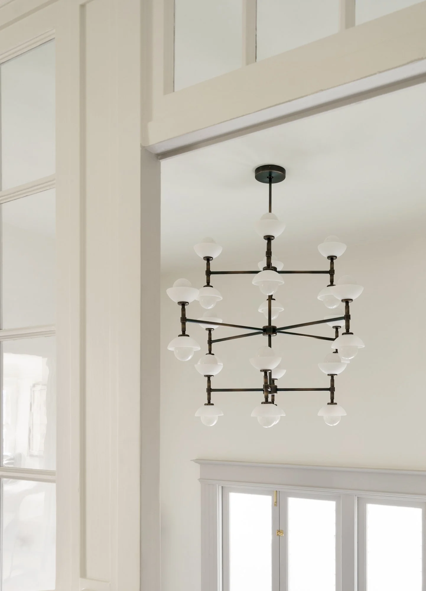 Modern geometric chandelier with multiple white glass shades hanging in a spacious room with large windows.