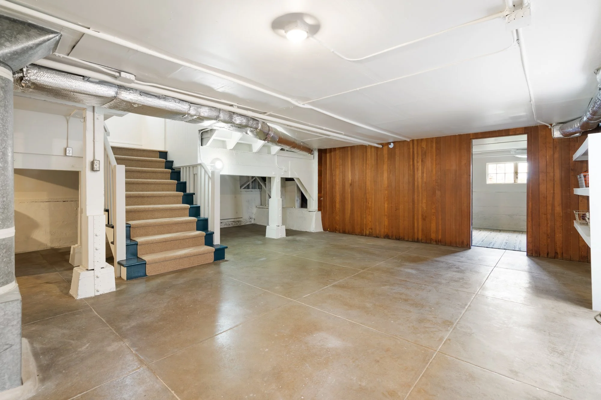 Unfinished basement with staircase, wood-paneled walls, and exposed ductwork.