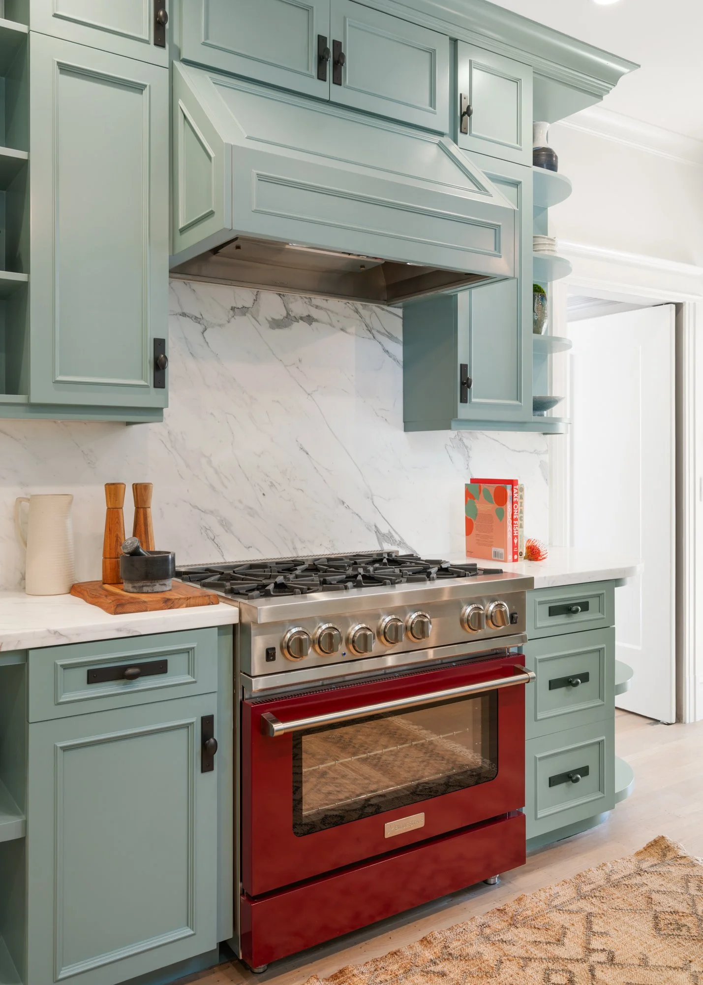 Modern kitchen with teal cabinets, red stove, marble backsplash, and wooden countertop accessories.