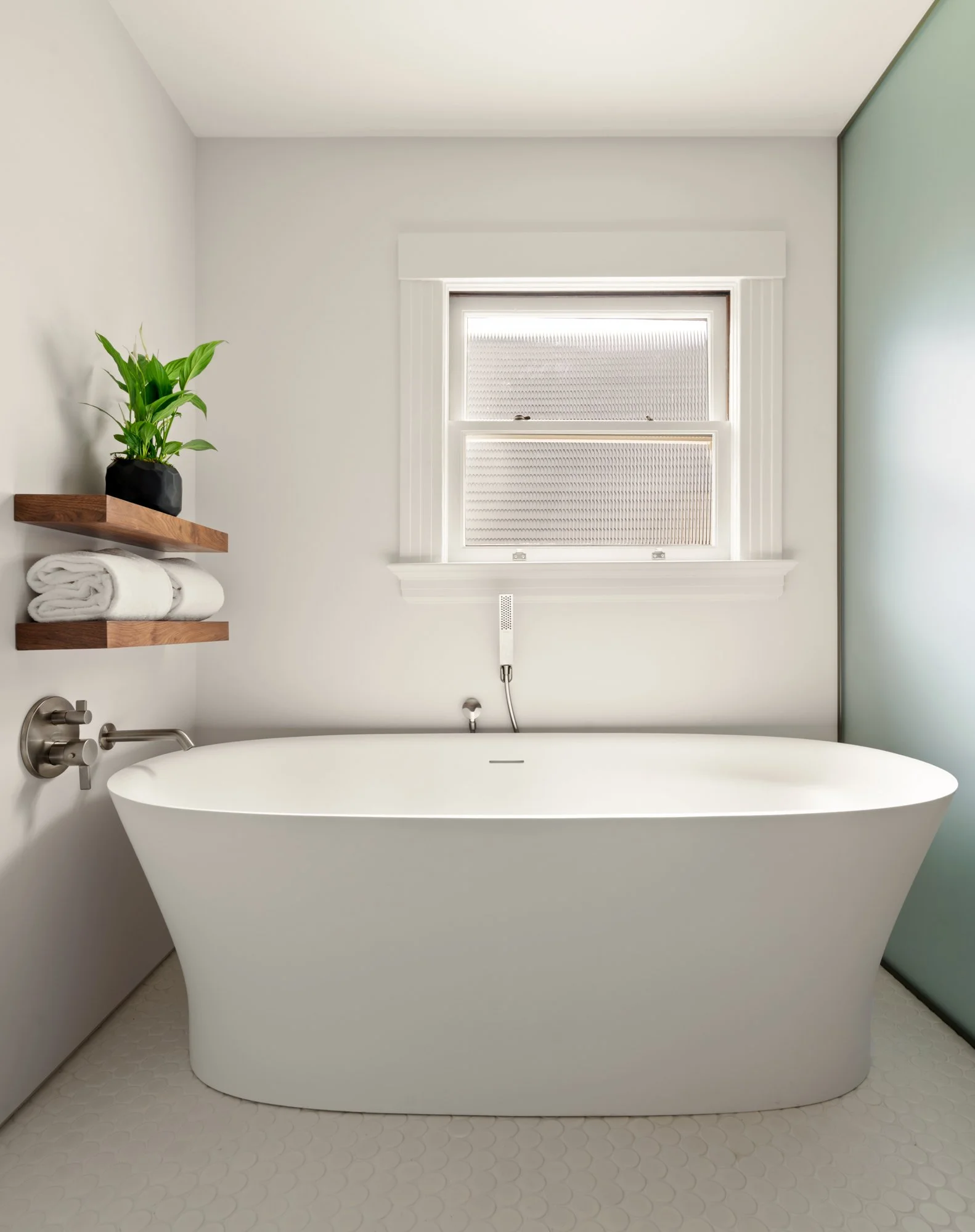 Modern bathroom with freestanding bathtub, window, shelves with towels, and a potted plant.