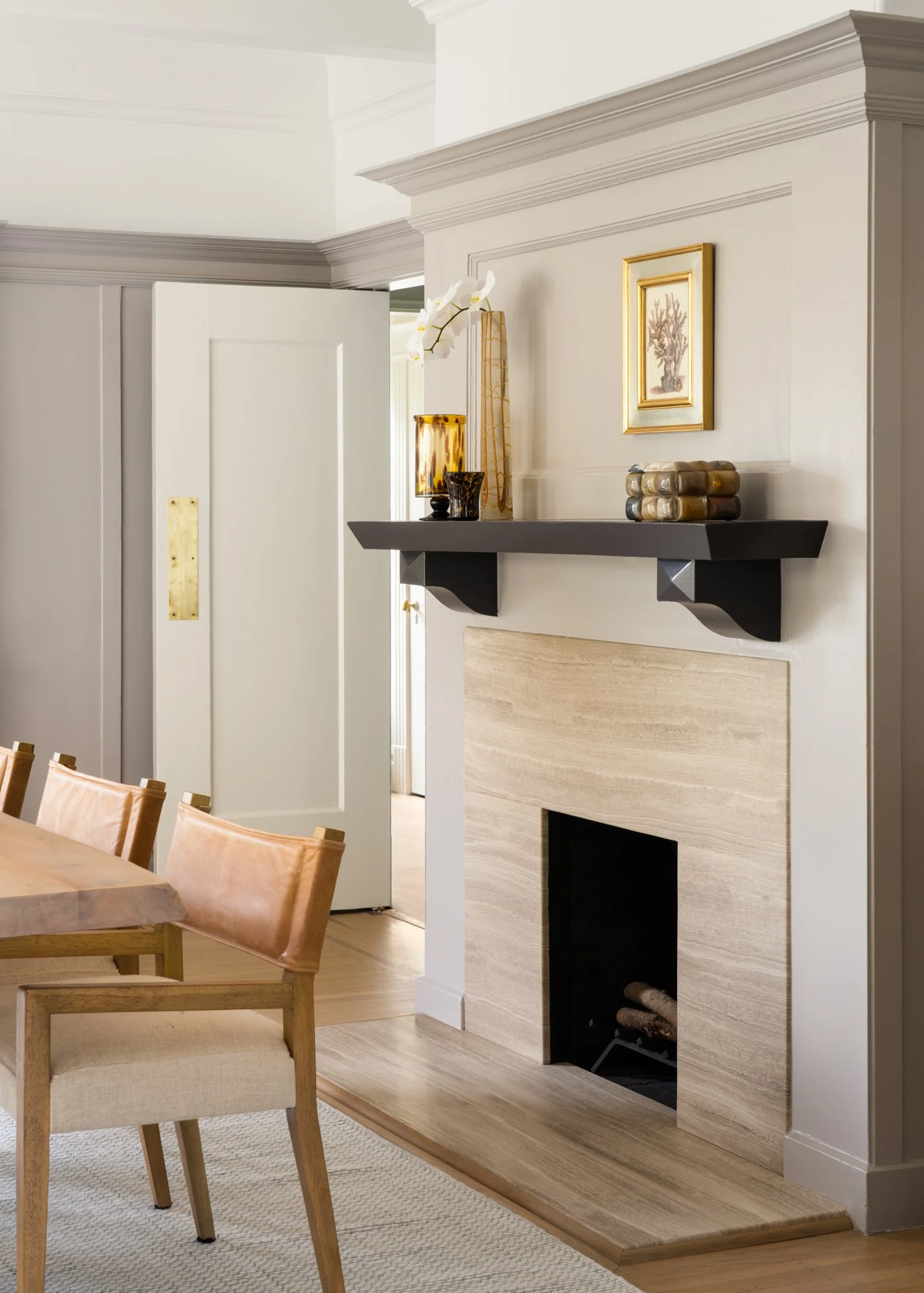 Modern living room interior with a beige fireplace, black shelf with decorative items, and wooden furniture in a neutral color palette.