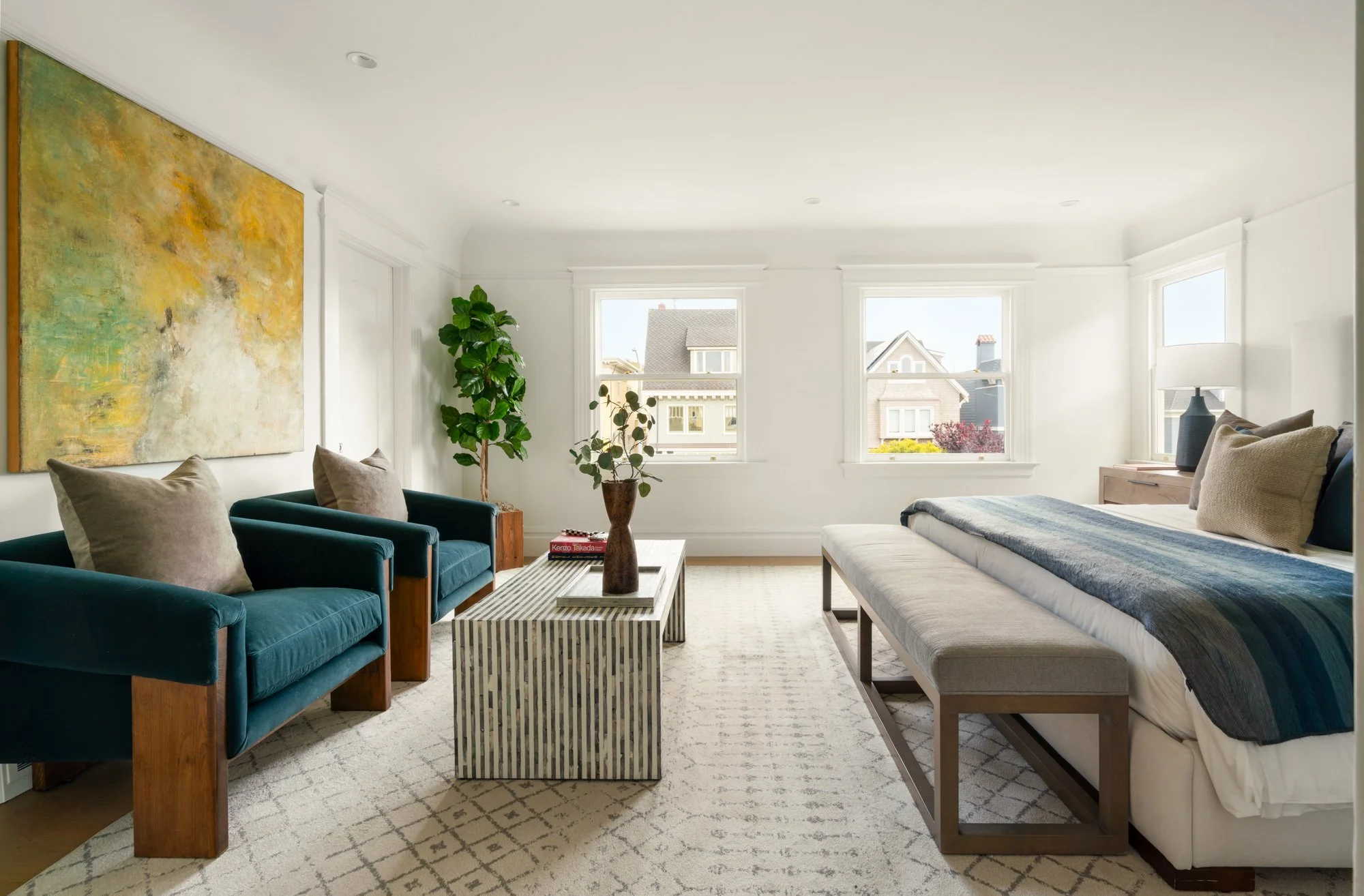 Bright minimalist bedroom with a bed, navy chairs, abstract art, striped coffee table, and large windows.