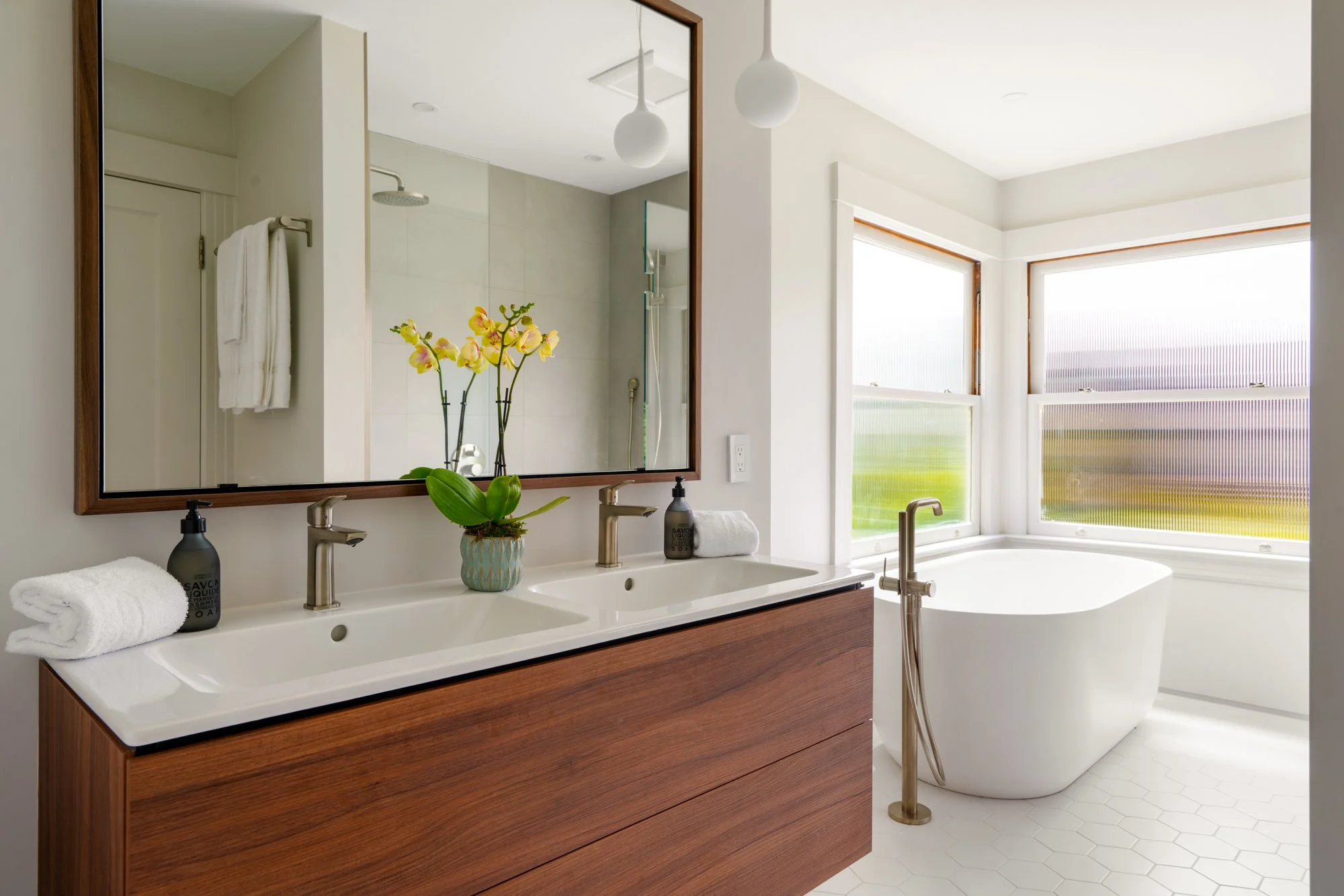 Modern bathroom with double sink vanity, large mirror, freestanding bathtub, and decorative orchid plant.