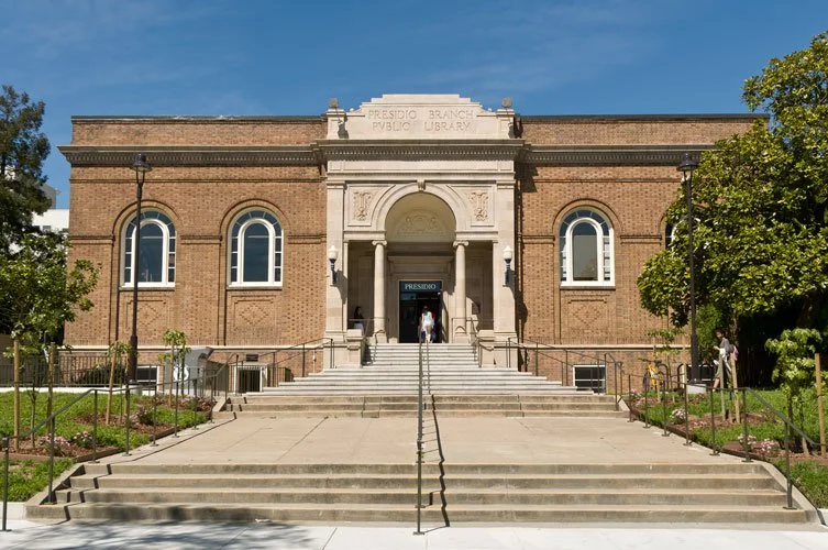 Facade of Presidio Branch Library, a historic brick building with arched windows and grand entrance, surrounded by greenery.