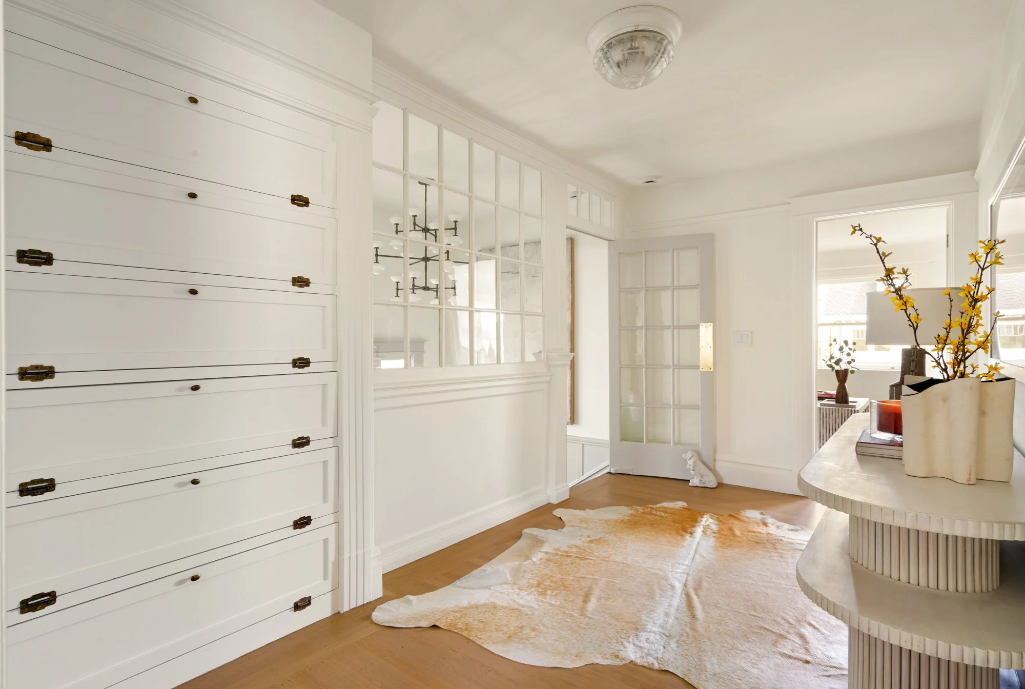 Modern interior with white built-in cabinets, glass-paned door, brown cowhide rug, and decorative table with flowers.