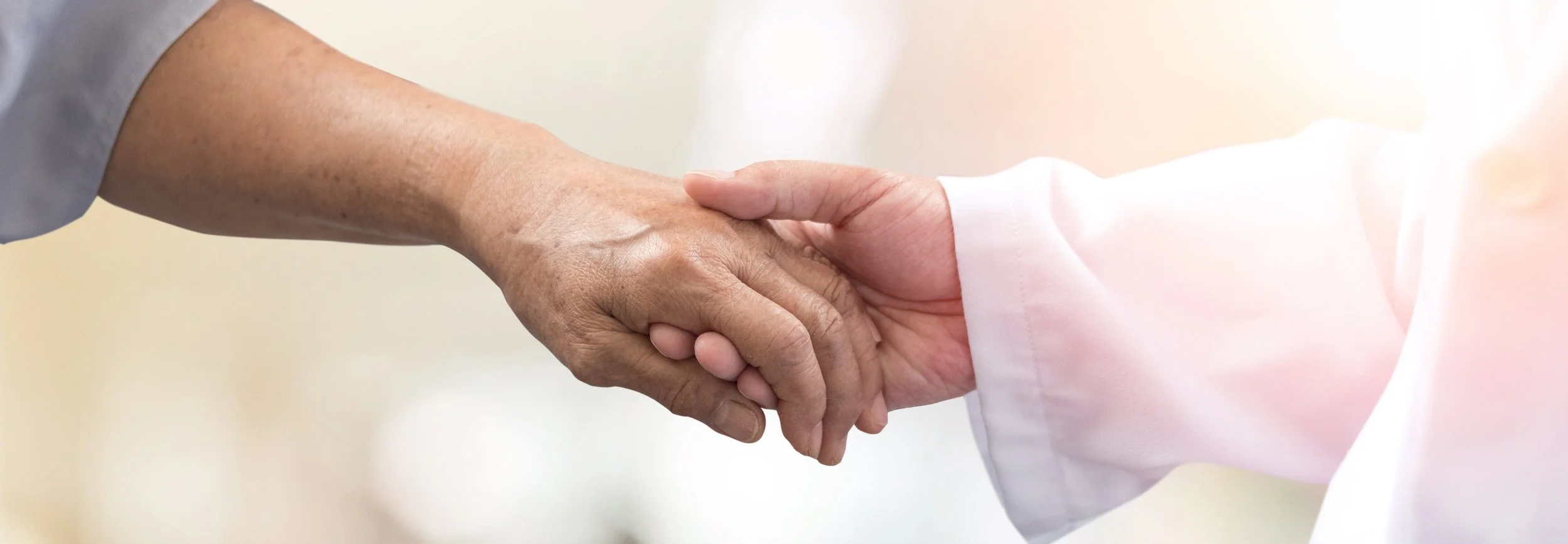 Two people shaking hands, one in a light gray shirt and the other in a white coat, possibly in a professional or medical setting.