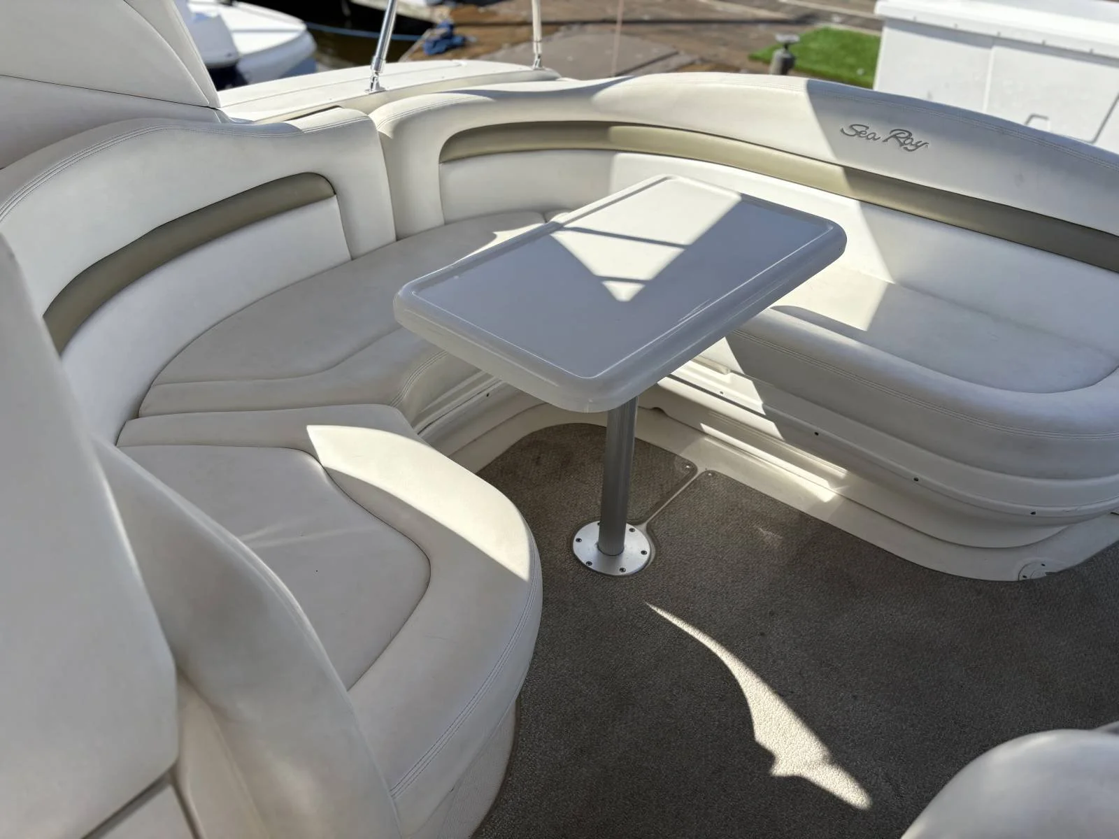 White cushioned seating area on a boat with a small rectangular table in the center, with the words 'Sea Ray' embroidered on the upper right side.