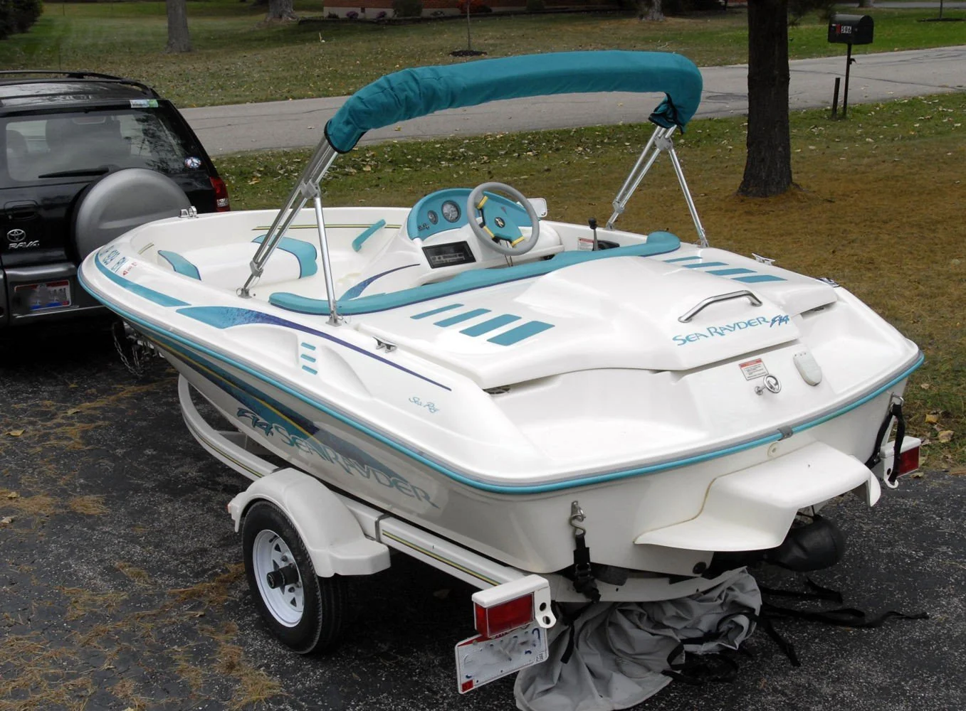 White Sea Rayder speedboat on a trailer attached to a vehicle, parked on a driveway with trees and a grassy area in the background.