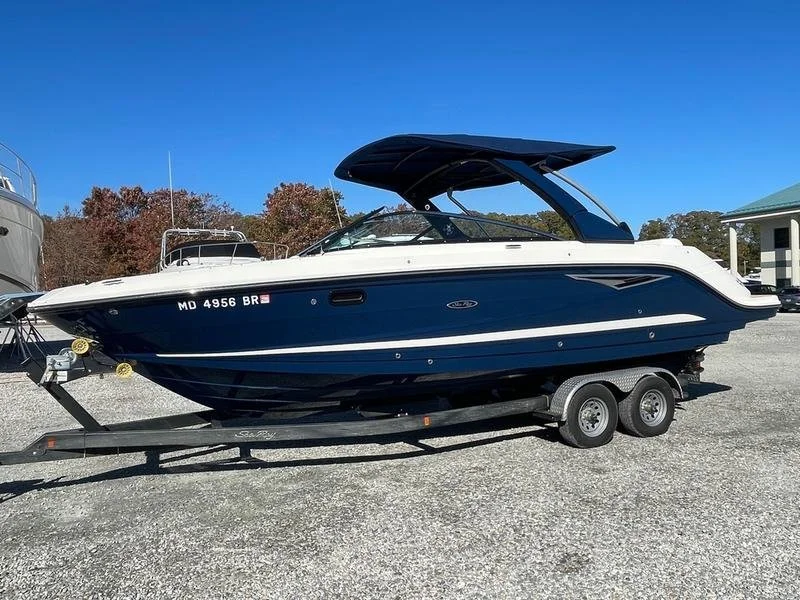 A blue and white motorboat on a trailer at a boat yard with trees and a building in the background. Boat pictured is a 2022 Sea Ray 280 SLX.