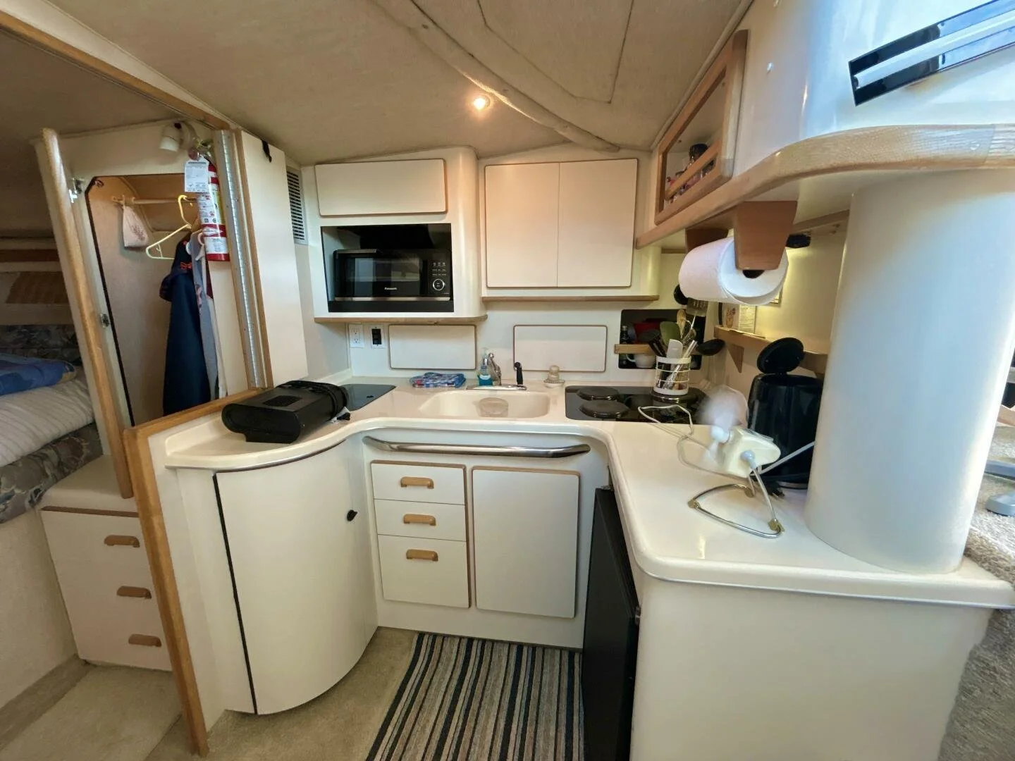Compact kitchen area inside a Sea Ray Sundancer boat, with white cabinets, a microwave, a small sink, stovetop, and various kitchen essentials.