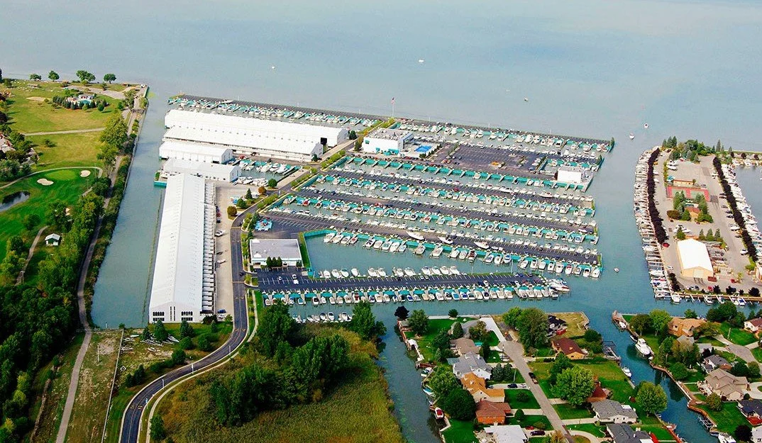 Aerial view of a marina with boats docked, adjacent to a residential neighborhood, on a body of water. MacRay Harbor, a marina on Lake St. Clair in Michigan.
