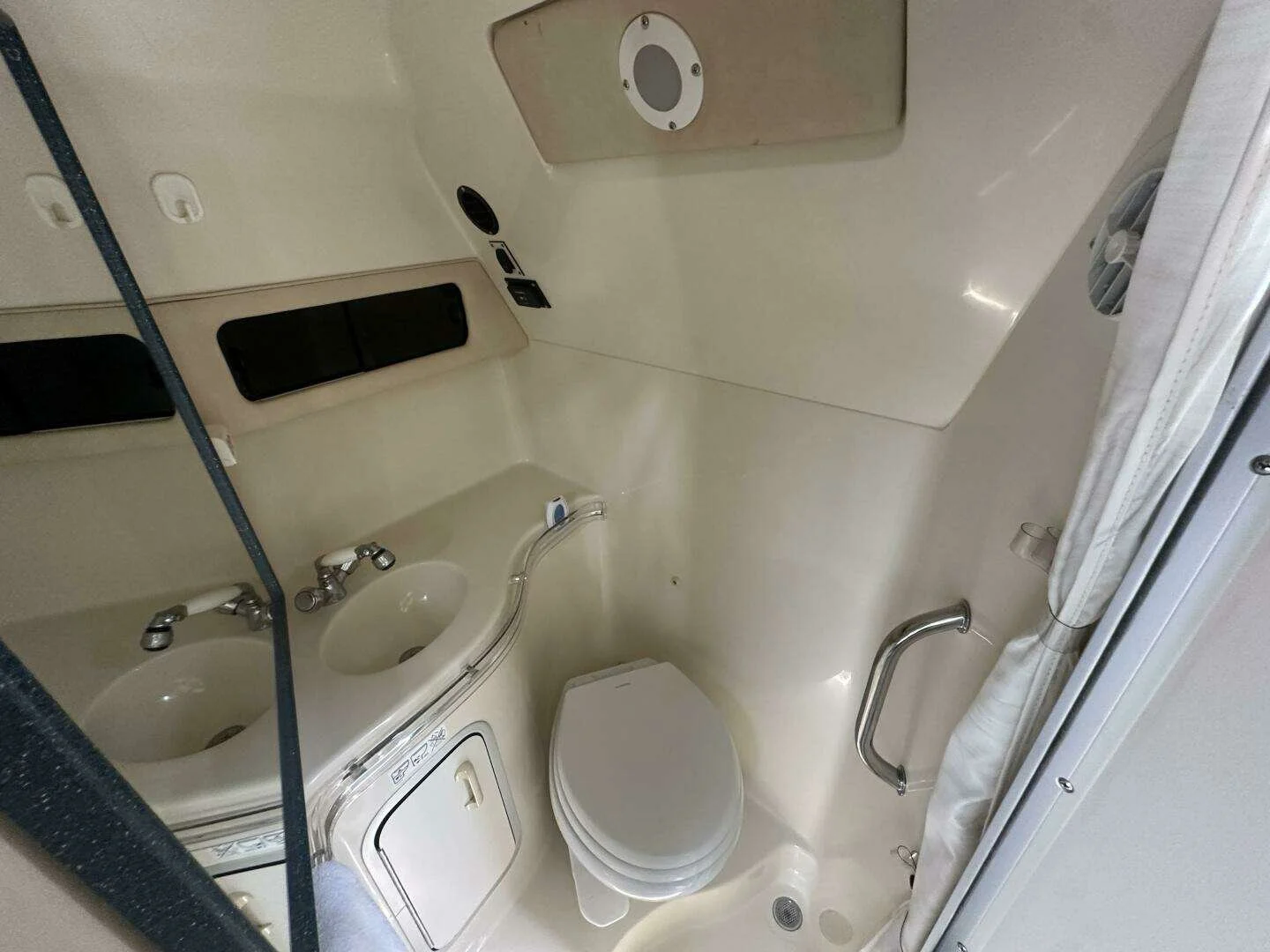 Washroom / head on a boat,  containing a toilet, a sink with faucet, a mirror, and safety bars, with beige walls and compact fixtures. Sea Ray Sundancer.
