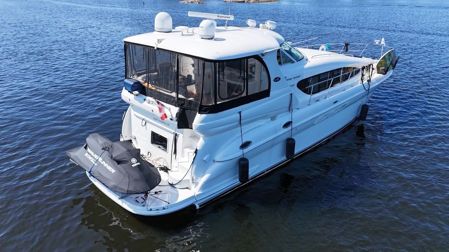A white yacht on calm water with a covered outdoor deck, antennas, and a small inflatable boat at the stern.