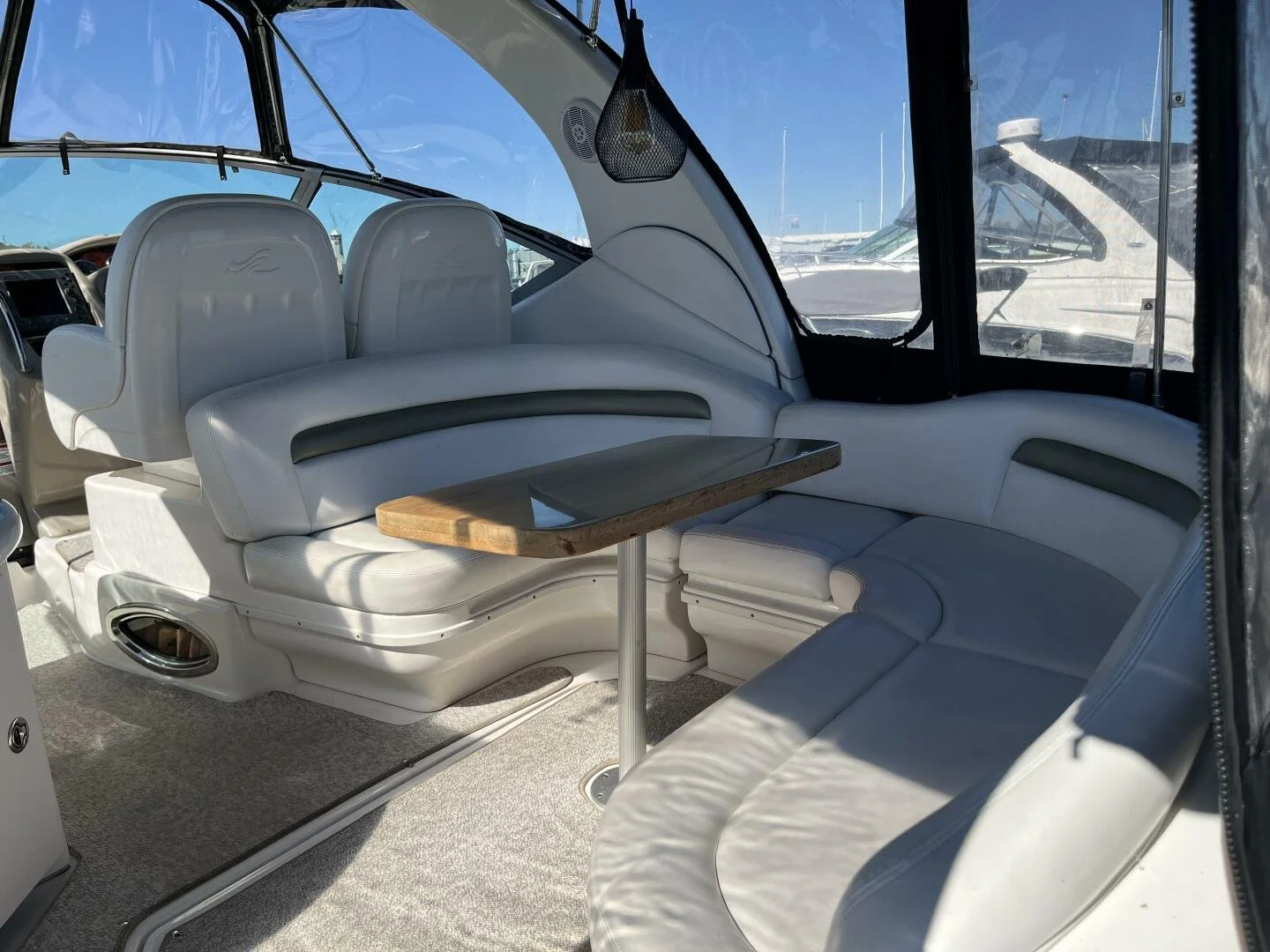 Cockpit on Sea Ray 340 Sundancer, with white leather seating, a wooden table, black cockpit canvas and windows showing other boats docked outside.