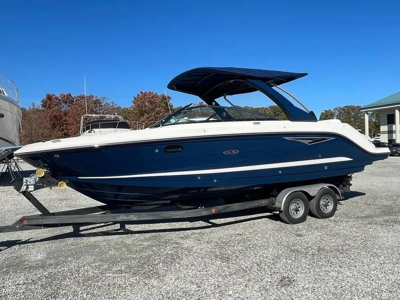 A blue and white motorboat on a trailer in a gravel lot.